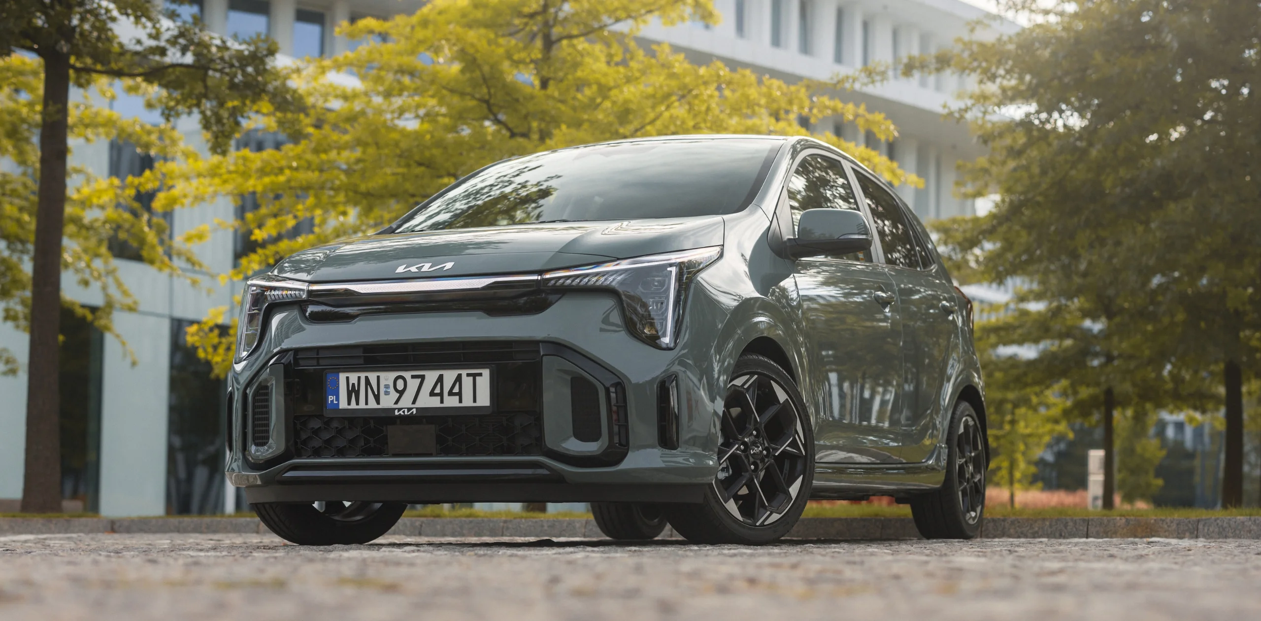 Kia Picanto glo – nowoczesny, kompaktowy hatchback w miejskim stylu, widok z przodu i boku na tle drzew